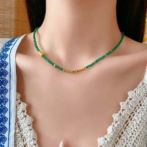 Gros plan des perles vertes et détails dorés sur un collier en acier inoxydable
