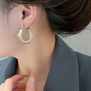 Close-up of a silver-toned hexagonal hoop earring on a model for a modern minimalist style