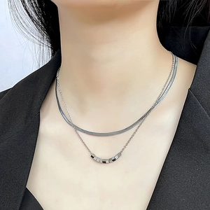 Detail of a double-layered silver necklace with snake chain and geometric cube beads
