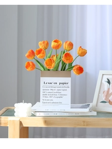 Detail of lifelike orange PU tulips in a French paper bag with books and candles