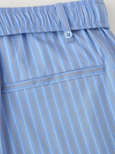 Detail of blue striped trousers featuring elastic waist with button and welt pocket