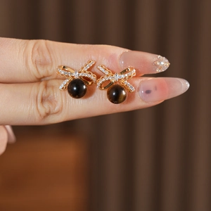 Detailed view of gold bow earrings with crystals and brown tiger eye bead held on fingers