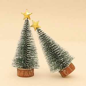 Miniature green frosted Christmas trees with gold stars and wooden bases on beige background