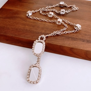 Macro shot of rose gold glasses pendant necklace with zircon inlay on a wooden tray