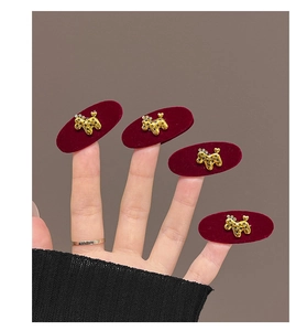 Detail of four golden poodle hair clips with stars on red velvet bases held by hand