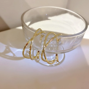 Macro detail of gold-finish intertwined hoop earrings with hammered texture on glass