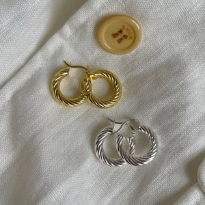 Close-up of twisted hoop earrings in gold and silver finish on natural linen texture