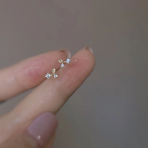Mini gold cherry stud earrings with three clear zircons held on a fingertip