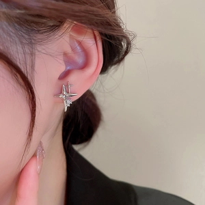 Close-up of a silver four-pointed star earring with a center crystal on a model's ear