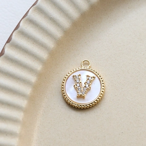 Close-up of a gold-plated shell pendant with zircon letter V inlay on a ceramic plate