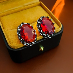 Macro detail of oval red ruby earrings in vintage dark metal setting inside luxury box