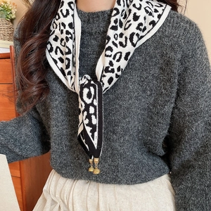 Detail of leopard print knitted shawl with gold bell pendant on a fuzzy sweater