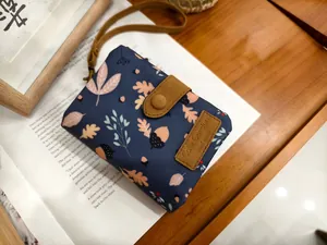 Detail of navy canvas leaf print wallet with leather buckle and brand tag on desk