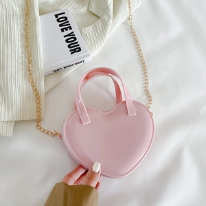 Pink heart-shaped crossbody jelly bag with gold chain strap on white fabric