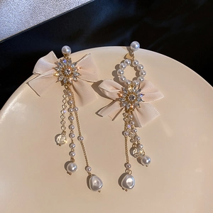 Detail of elegant bow tassel earrings with crystals and pearls on a white plate