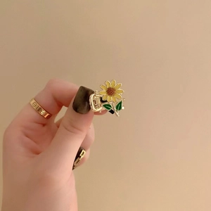 Detailed close-up of a small sunflower hair clip with green leaves on a gold metal base