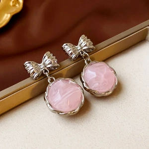 Dettaglio orecchini a fiocco argento con resina rosa su vassoio dorato di classe