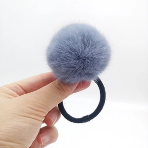 Detail view of a large blue-grey faux fur pom-pom hair tie with elastic black band