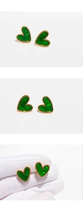 Detailed macro view of green heart stud earrings with gold trim held for scale