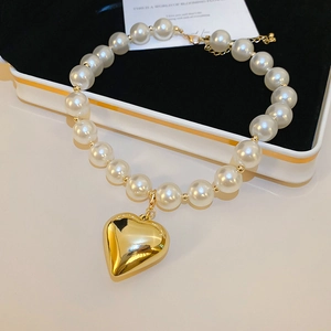 Detail of white pearl necklace featuring a polished gold heart pendant and lobster clasp