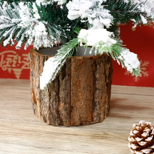 Mini snowy Christmas tree in natural bark planter with pine cones on wooden table