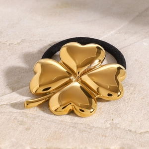 Golden clover hair tie made of polished stainless steel with black elastic band on stone