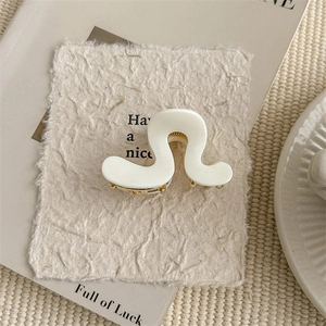 Close-up of a cream wavy hair claw clip with golden metal teeth on textured paper