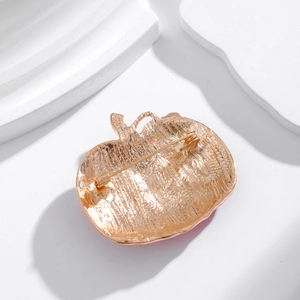 Back view of a gold metal apple brooch with a secure pin clasp and textured surface