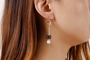 Detail view of long rose gold earrings with black infinity charm and white pearl on model