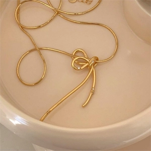 Detailed close-up of a gold-plated ribbon bow necklace with micro-pave crystals on a dish