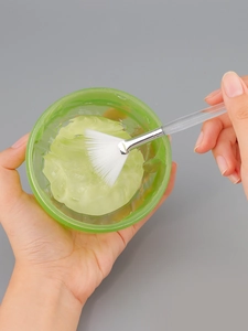 Applying facial mask gel with a white fan-shaped brush for professional skin care therapy