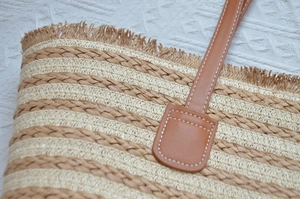 Detailed close-up of brown leather handles with contrast stitching on straw tote bag