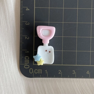 Macro detail of a 2.5cm resin shovel charm with smiley face on a centimeter scale pad