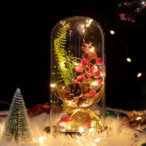 Detail view of a glass dome with LED lights, pine cones and red berries on plush surface
