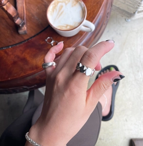 Lifestyle shot of irregular silver ring and woven bracelet on hand with coffee cup