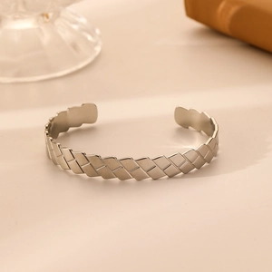 Detail shot of silver stainless steel open cuff bracelet with woven texture on beige surface