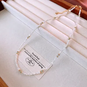 Elegant shell bead necklace with green gemstones and gold accents on a white velvet tray