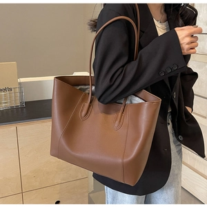 Brown leather tote bag worn with black blazer, showing large capacity and commuter style