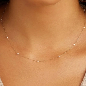 Detailed close-up of a delicate gold chain necklace featuring small spaced white pearls