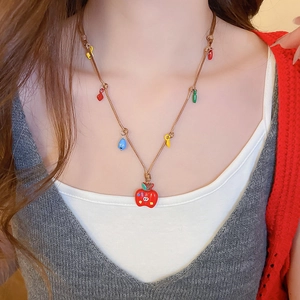 Gros plan d'un collier pendentif pomme avec breloques colorées sur un cordon tressé brun