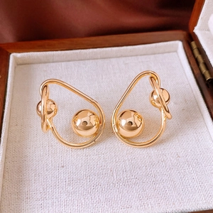 Détail des boucles d'oreilles boules dorées torsadées dans une boîte à bijoux en bois