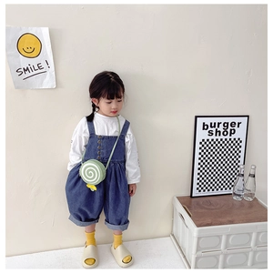 Detail of a kids lollipop-shaped crossbody bag paired with denim overalls and a white top