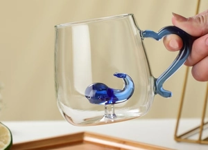 Detail of creative glass mug with 3D blue whale sculpture and ergonomic handle
