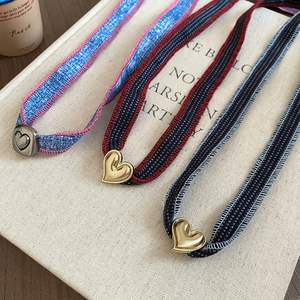 Detail of woven denim heart pendant necklace on a cream vintage book background