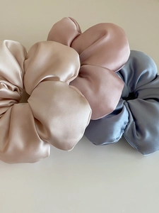 Detailed view of three large satin scrunchies in champagne gold, lotus pink, and misty blue