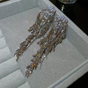 Detail of silver tassel earrings with rectangular zircons and hanging leaf charms on velvet