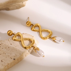 Détail de boucles d'oreilles symbole infini doré avec perle goutte blanche sur pierre