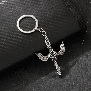 Close-up of gothic silver keychain with cross rose and wings on textured surface