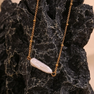 Detail of a 18K gold-plated necklace with Baroque pearl on a textured rock background