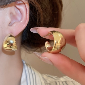 Detail view of chunky golden C-shape hoop earrings showing thickness and glossy finish